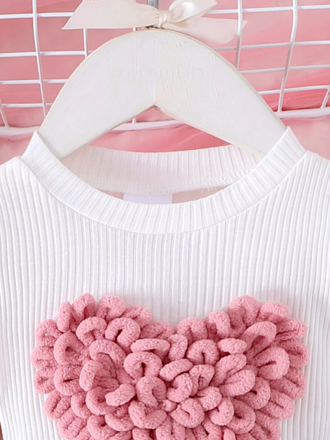 White sweater with a pink textured heart design on a hanger against a pink background