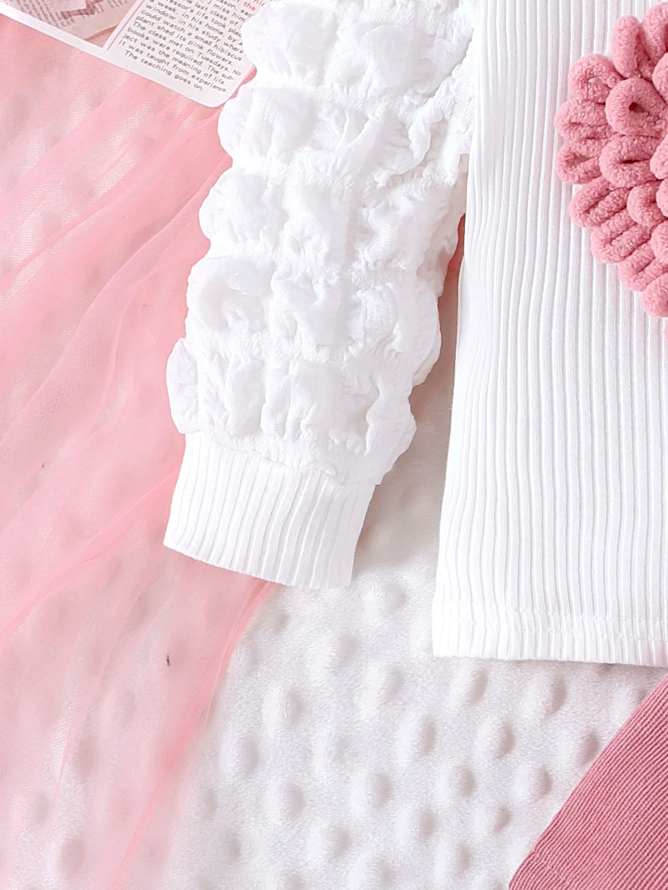 White textured sweater on a pink surface with a pink flower and white text.